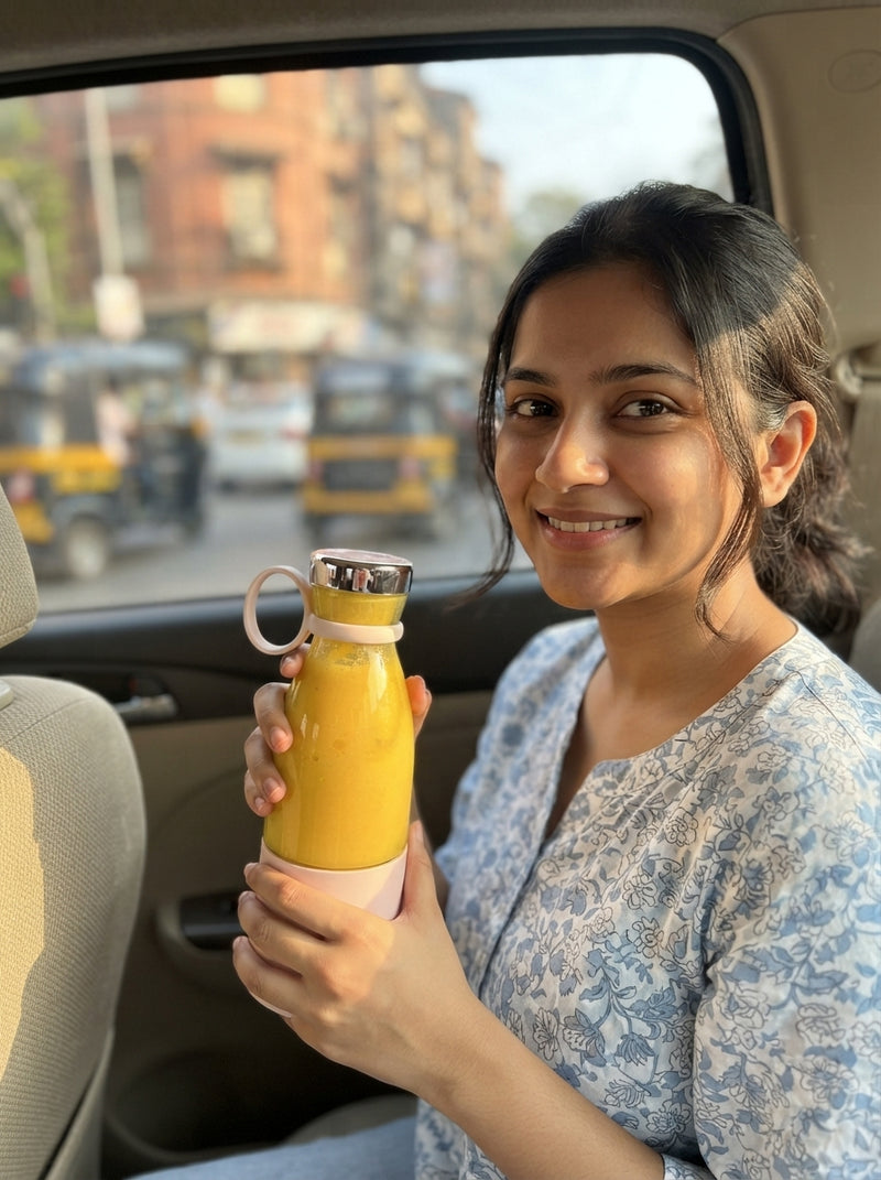 A woman in a car holding a portable blender filled with a fresh mango shake while sitting in Mumbai traffic.